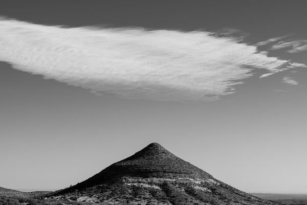 Black and white landscape photograph of a pointed mountain peak with a cloud above it found in the western desert near Ft. Davis, Texas.