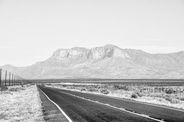 Black and white landscape photograph of a lonesome highway through the vast silent desert.