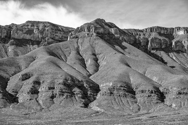 Black and white landscape photograph of an amazing mountain range with deep folds of Earth rising to sheer rocky cliffs and barren peaks.
