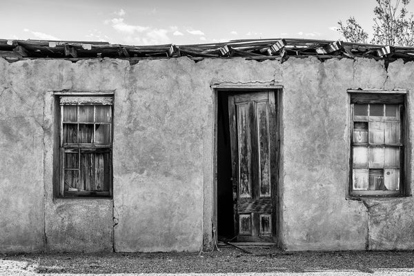 Black and white photograph of the front of a ruined adobe house in a small desert community near Marfa, Texas.