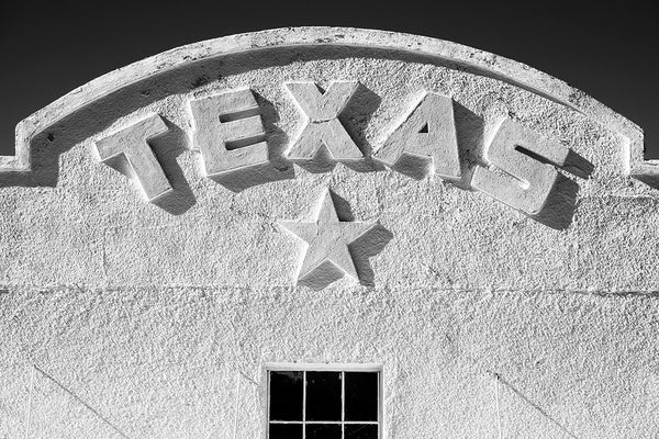 Black and white photograph of the word Texas on an arch and a lone star on the front of the old Texas Theater in Marfa, Texas.