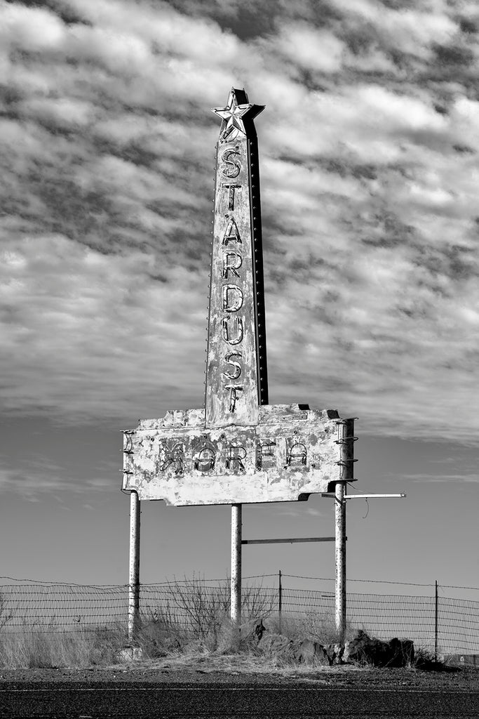 Black and white photograph of the faded old Stardust Motel sign seen on the side of a desert highway near Marfa, Texas.