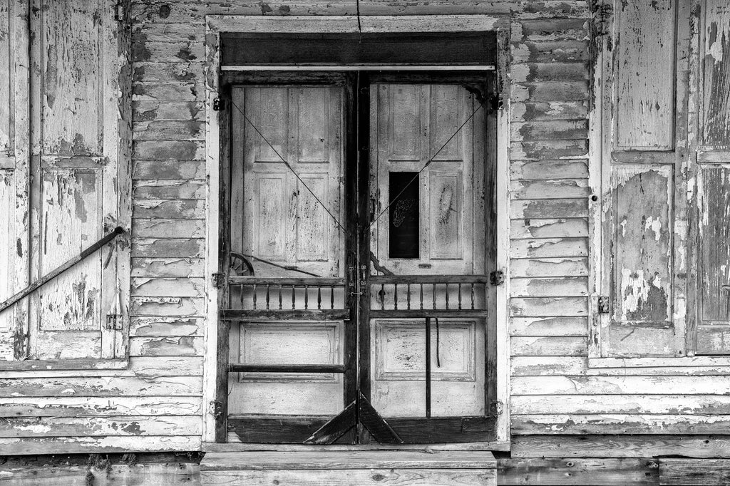 Black and white photograph of tattered screen doors on the front of an abandoned country store found along a back road.