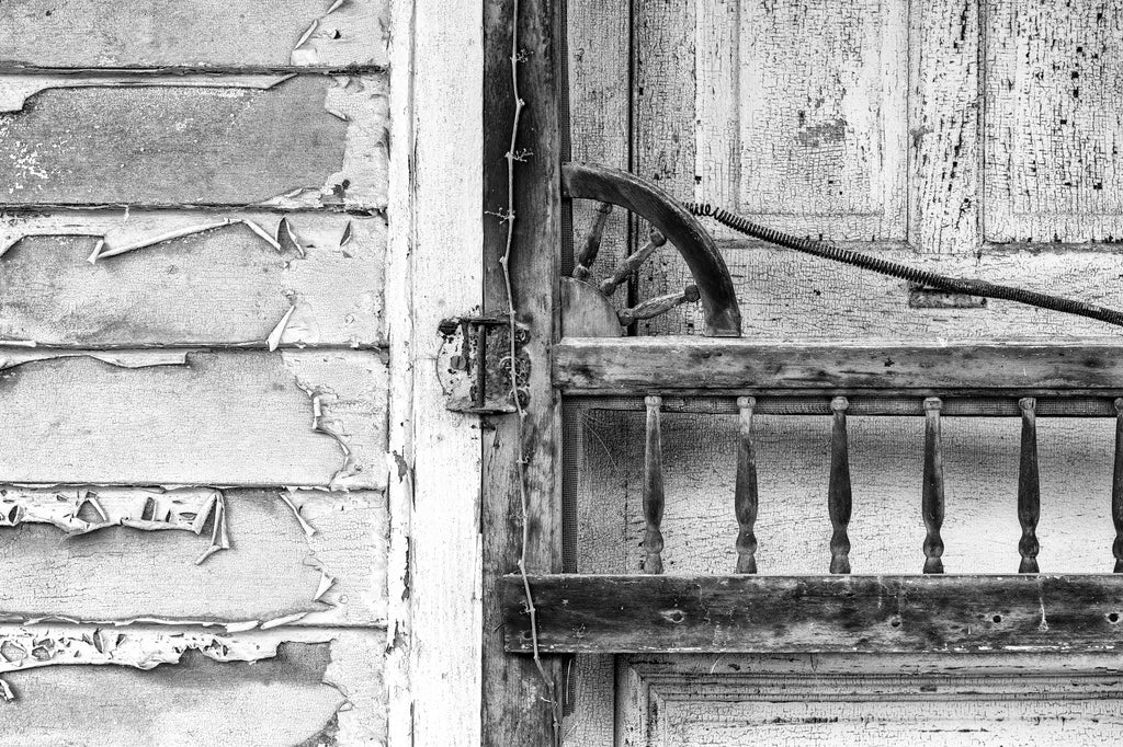 Black and white detail photograph of the doors and peeling paint on the clapboards of an abandoned old country store found along a back road.