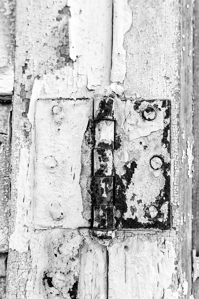 Black and white detail photograph of a rusty door hinge on an abandoned building.