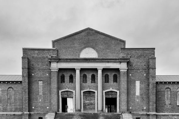 Black and white photograph of a majestic but abandoned building on a vacant college campus in the American South.