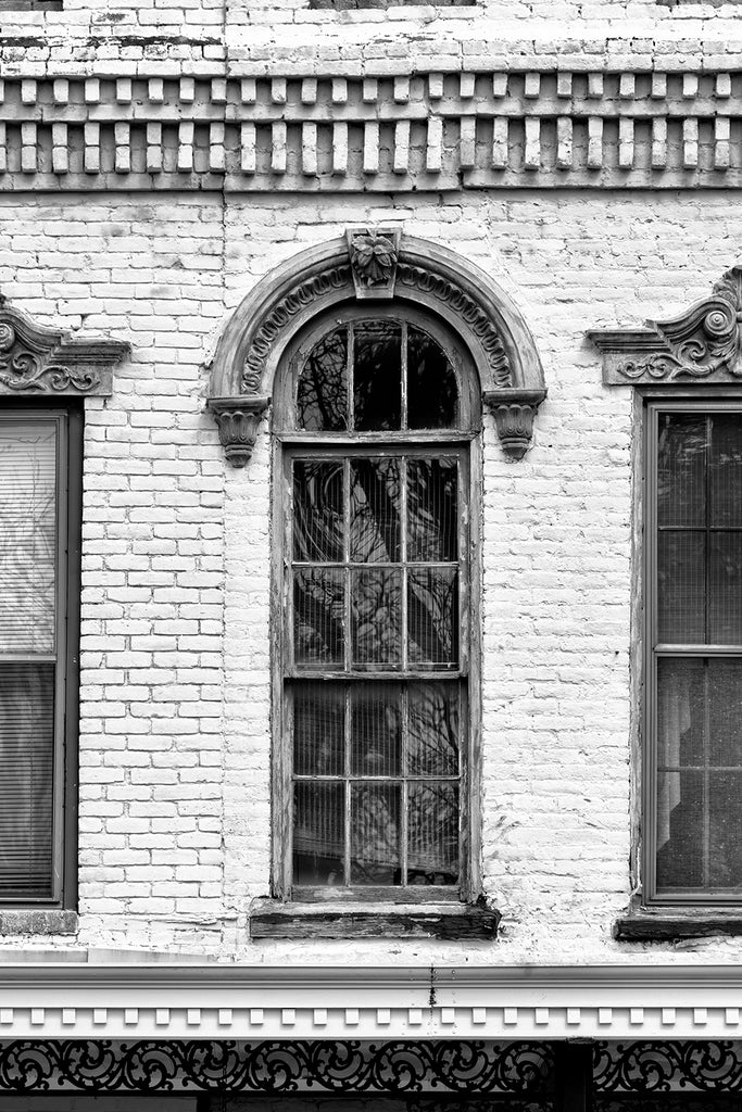 Black and white photograph of an ornate window with a decorative arch in an antique brick building.