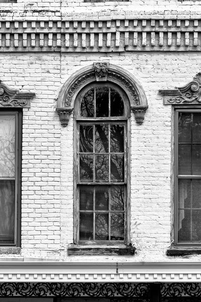 Black and white photograph of an ornate window with a decorative arch in an antique brick building.