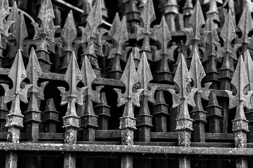 Black and white photograph of the pointed finials on stacks of old ironwork fences that have been removed and placed into storage.