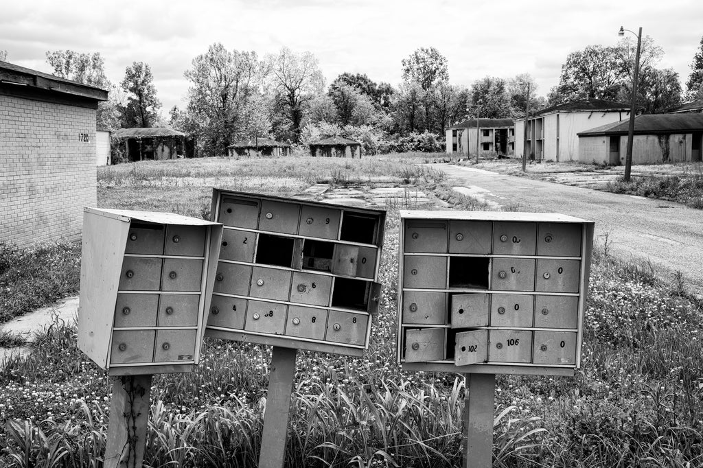 Black and white photograph of a block of broken mailboxes in the midst of an abandoned and silent apartment complex.