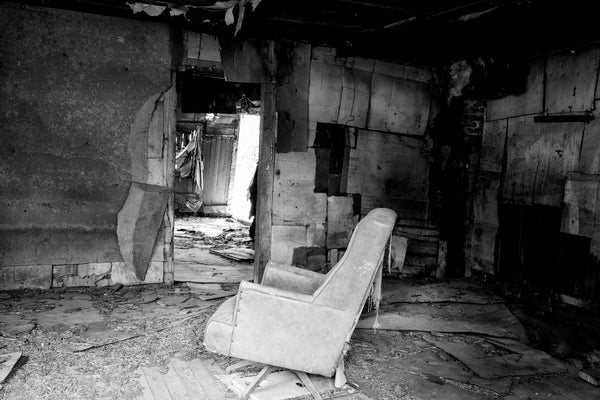 Black and white photograph of an old chair that was left inside a ramshackle abandoned old house.