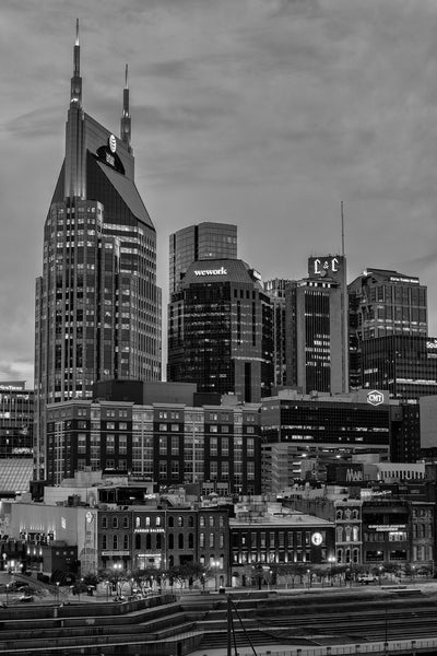 Black and white photograph of the old and new Nashville skyline at twilight, as seen from the pedestrian bridge.