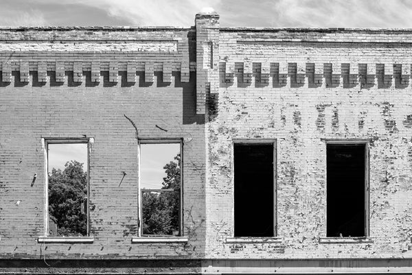 Black and white photograph of the windows of two historic, abandoned storefront buildings in a small town in the deep south.