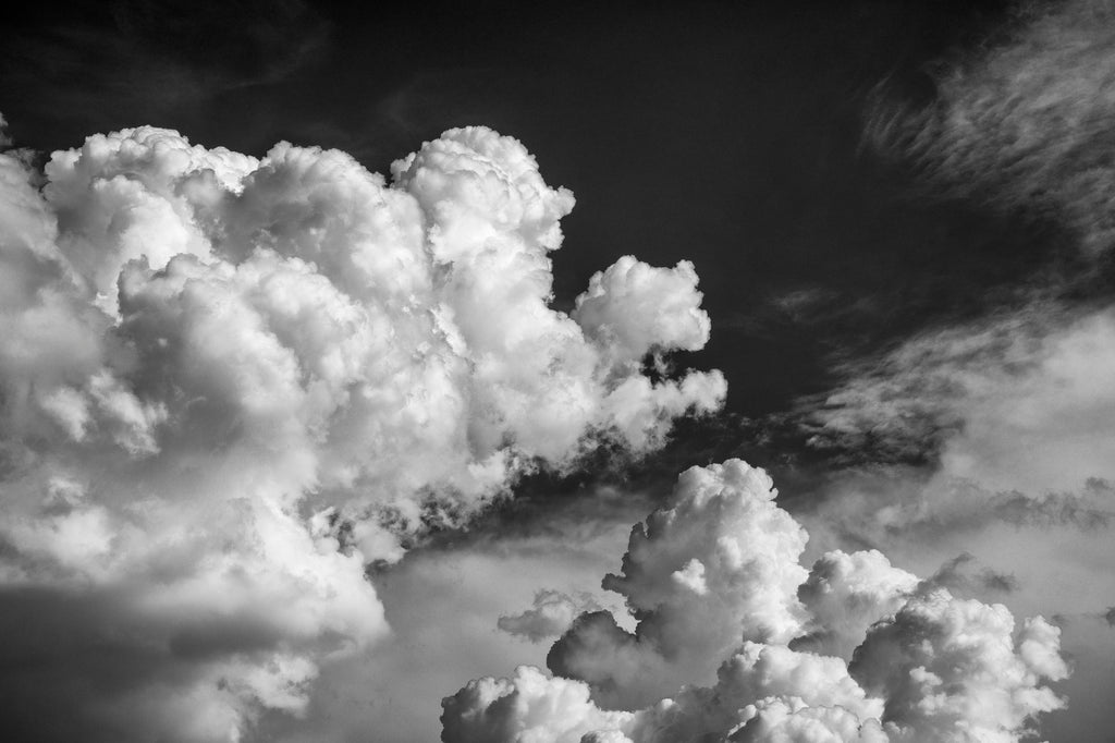 Black and white photograph of tumultuous summer cloud banks exploding upwards into the deep blue sky.