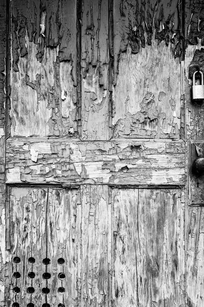 Black and white photograph of the weathered front door of an abandoned building covered in the texture of cracked and peeling paint.
