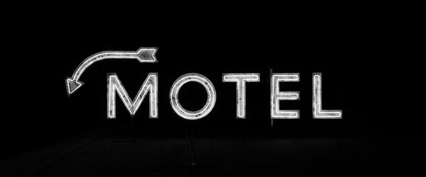 Black and white photograph of a vintage neon sign for an old roadside motel featuring an arrow pointing downward.