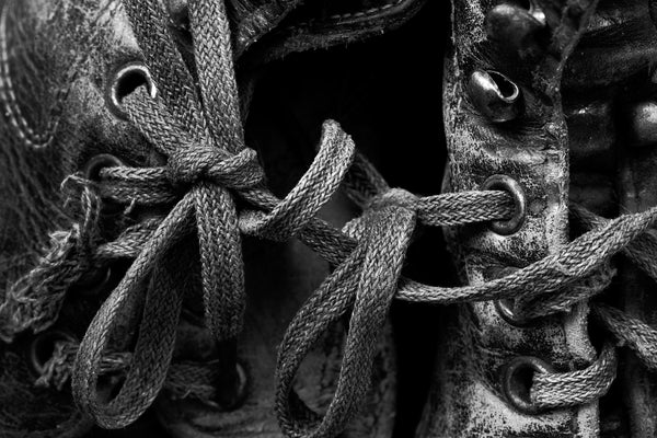 Black and white detail photograph of the laces of two old tattered leather boots tied together into loops, creating a beautiful composition.