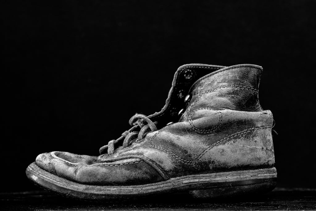 Dramatic black and white photograph of a worn-out old leather boot.