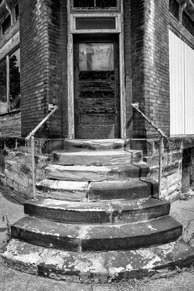 Black and white photograph of a stack of rounded stone steps leading up to the front door of an abandoned old building in South Wheeling, West Virginia. Built in 1901, it was the location of Holdermann Bros. grocery store in 1919, and later held residential units upstairs.