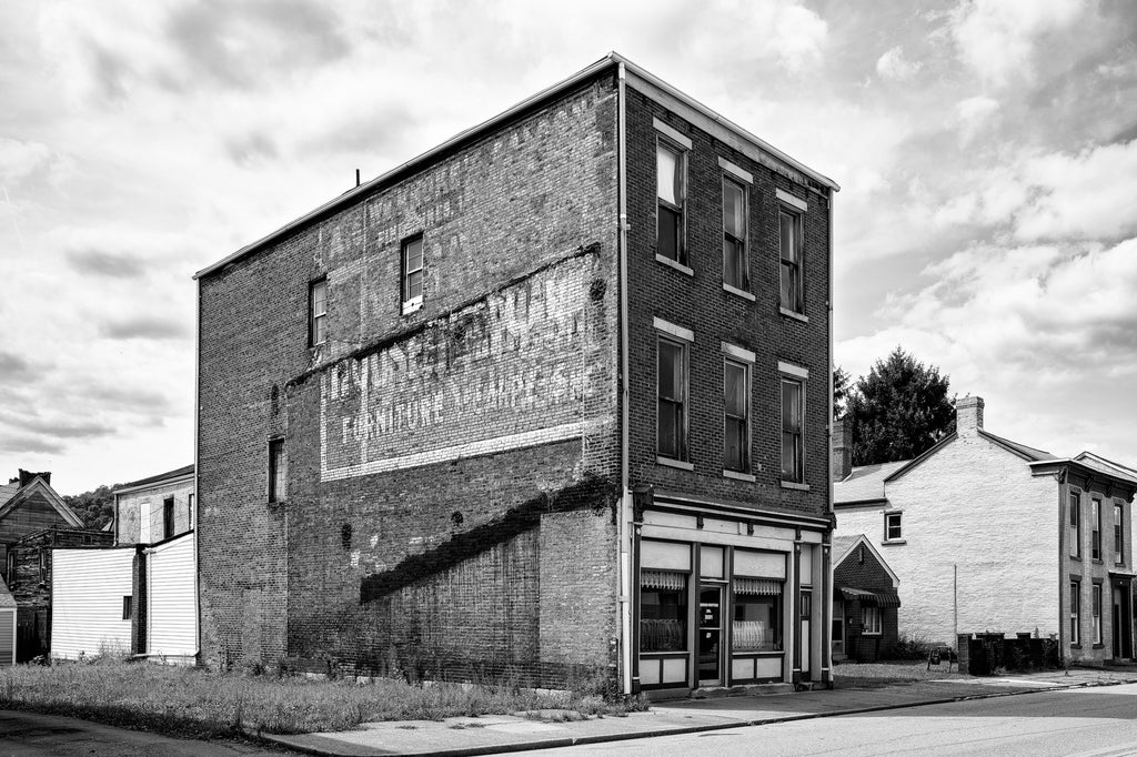 Black and white photograph of a three story brick building with layers of fading vintage wall ads on its side, seen in South Wheeling, West Virginia.