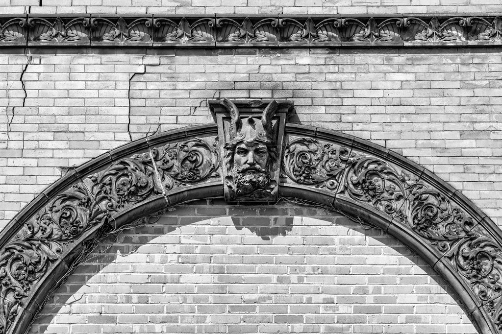 Black and white photograph of architectural details featuring a human head wearing a winged helmet on the exterior of the historic Schmulbach Brewing Company. Founded as the Nail City Brewery in 1855, it was acquired by investors in 1873. Majority partner Henry Schmulbach changed the name in 1882 and hired a master brewer from the famous Gambrinus Brewery in Cincinnati. Schmulbach was closed in 1914 when West Virginia passed prohibition laws.