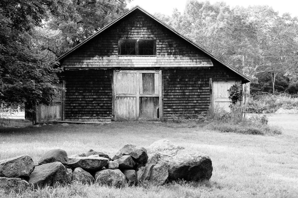 Black and white photograph of a historic old New England wooden barn with a stone wall in the foreground.
