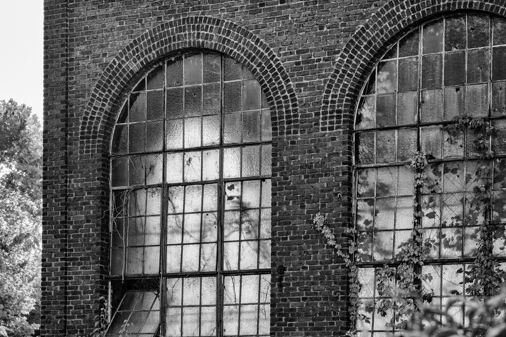 Black and white photograph of morning light glowing through the textured panes of old industrial mill windows.