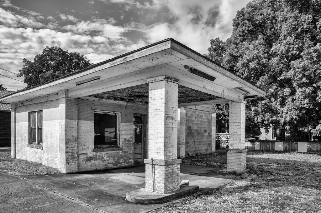 Black and white photograph of an abandoned old filling station on a street corner in a small Midwestern town.