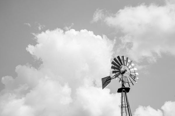 Black and white photograph of a windmill with towering clouds in the sky behind.