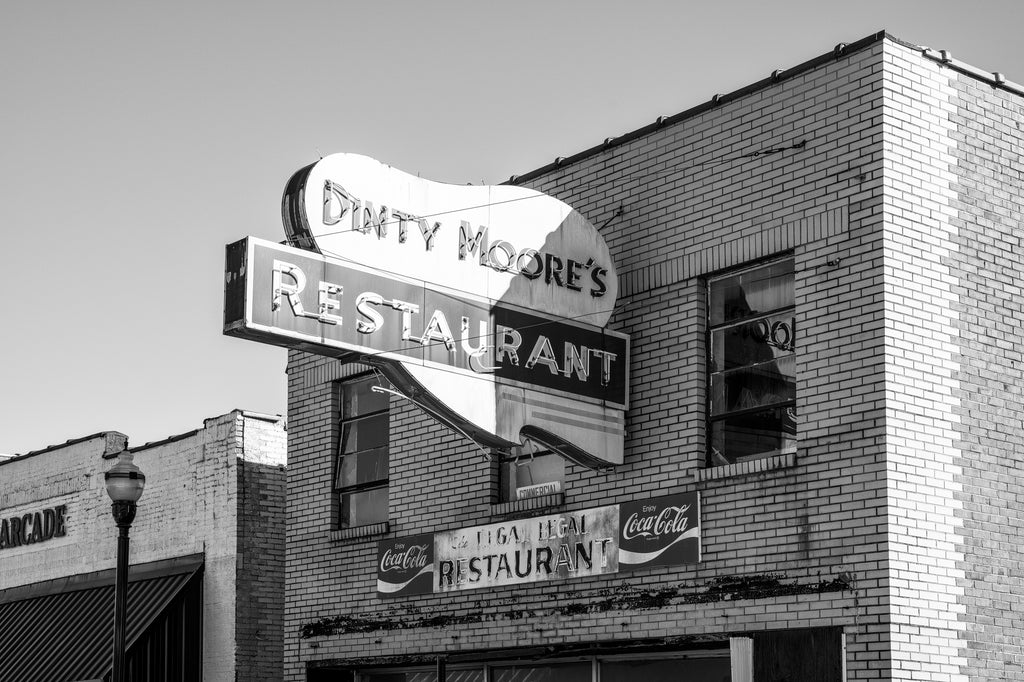 Black and white photograph of a vintage Dinty Moore Restaurant sign in McMinnville, Tennessee. Subsequent businesses have left the sign in place but the building is now vacant.