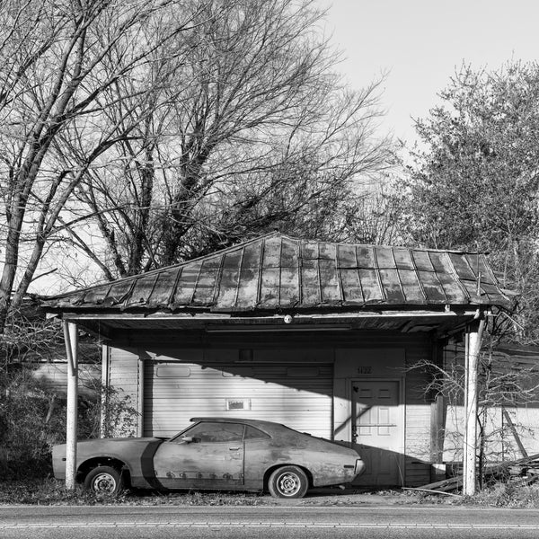 Black and white photograph of a classic car abandoned at the ruins of an old roadside service station that's now collapsing.