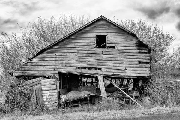 Black and white photograph of a beautifully derelict hay barn found alongside the pavement of a back road in the American South.