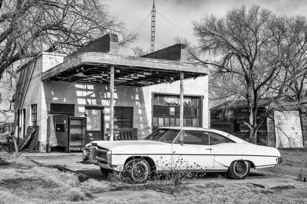 Black and white photograph of an abandoned art moderne gas station with a junked car on old Route 66. This was a Texaco station built in the 1950s and closed in the 1970s.