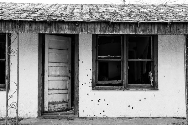 Black and white photograph of an abandoned old motel room riddled with bullet holes, found along old Route 66 in Glenrio, Texas.