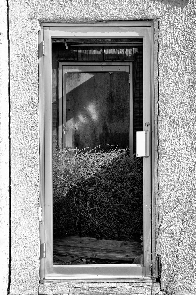 Black and white photograph of a tumbleweed held in the front entrance of an abandoned restaurant along a forgotten stretch of old Route 66 in Texas. The restaurant was part of a motel and gas station that flourished in the glory days of Route 66, but closed in the 1970s when Interstate 40 was opened a few miles away. 