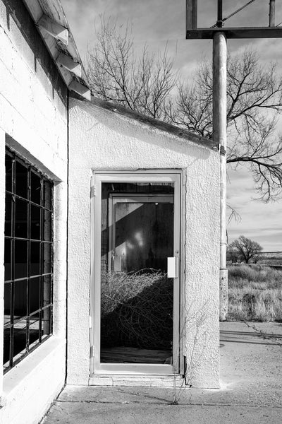 Black and white photograph of a tumbleweed trapped inside the entrance of an abandoned restaurant along a forgotten stretch of old Route 66 in Texas. The restaurant was part of a motel and gas station that flourished in the heydays of Route 66, but closed in the 1970s when Interstate 40 was opened a few miles away. 