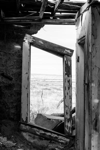 Black and white photograph of the New Mexico landscape seen through the broken window of an abandoned motel along old Route 66.