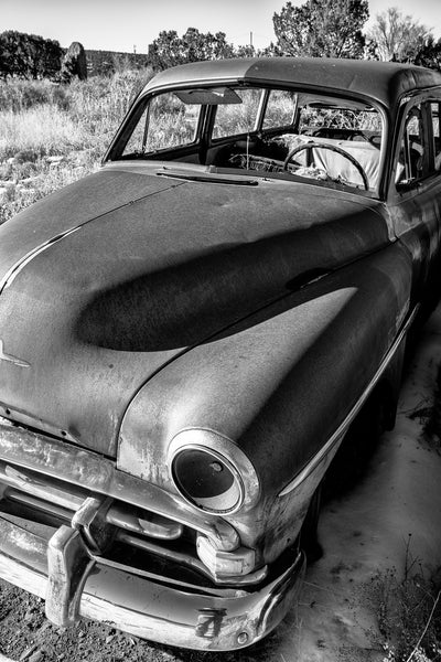 Black and white photograph of a rusty antique car abandoned in the New Mexico high desert landscape