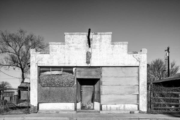 Black and white photograph of an abandoned building in Carrizozo, New Mexico with a very small object in the sky that looks very much like a UFO.