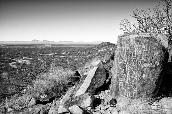 Black and white photograph of ancient petroglyphs in the landscape of New Mexico with the Tularosa Basin and San Andres Mountains in the distance.