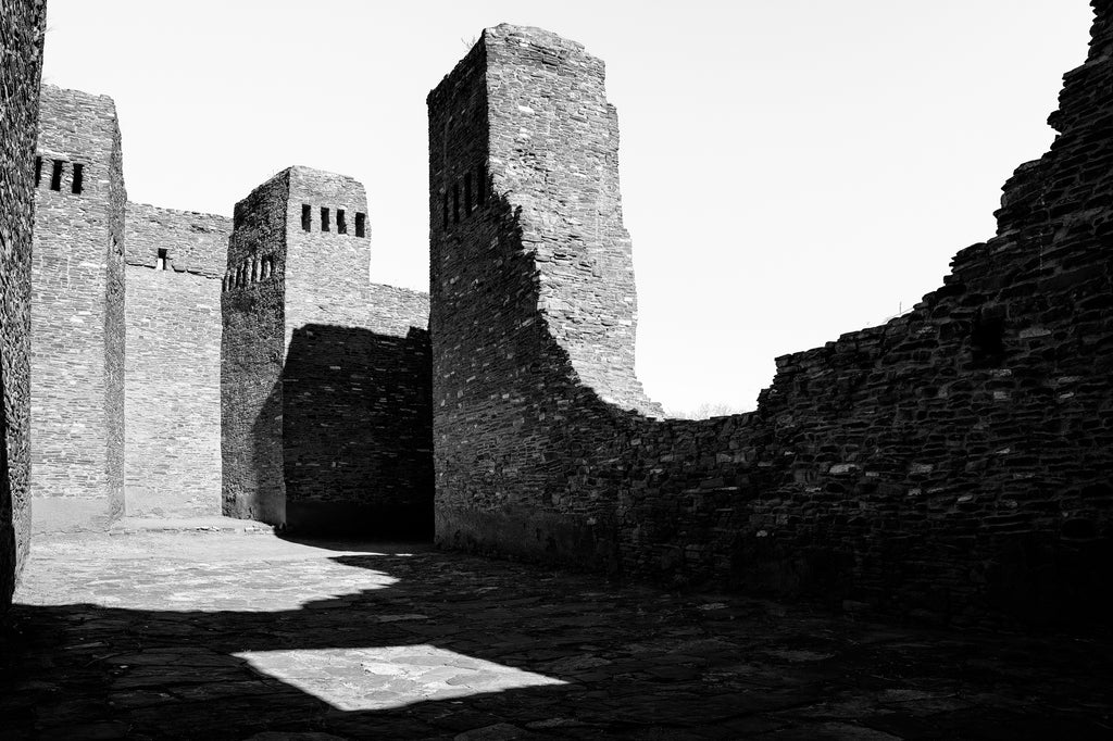Black and white photograph of towering stone ruins of an abandoned old stone church in the American Southwest. 