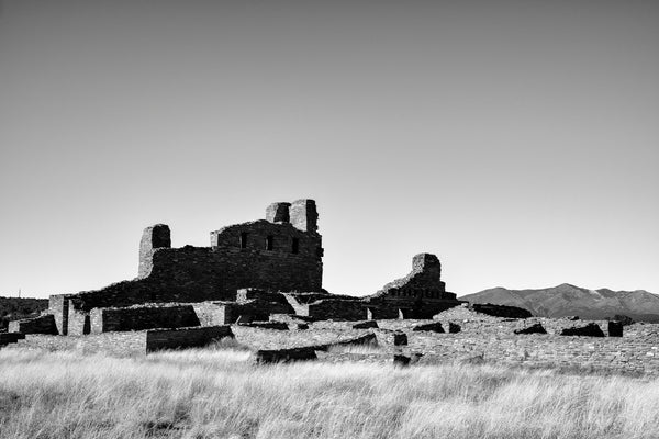Black and white photograph of the massive stone ruins of the 1600s-era Abó Pueblo Mission seen in the wide-open New Mexico landscape. 