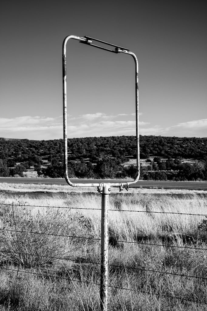 Black and white photograph showing an empty old roadside sign that frames the beautiful desert landscape of New Mexico.