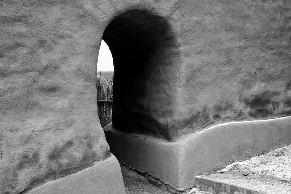 Black and white photograph of a portal through a thick wall in the ruins of an adobe church built 1717 in the Sangre de Cristo Mountains of New Mexico