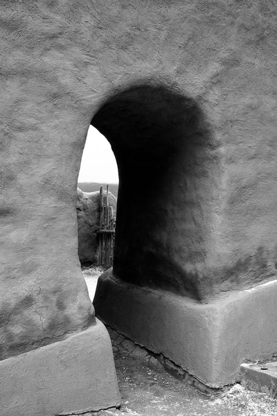 Black and white photograph of a doorway in the preserved ruins of an adobe church built 1717 in the Sangre de Cristo Mountains of New Mexico.