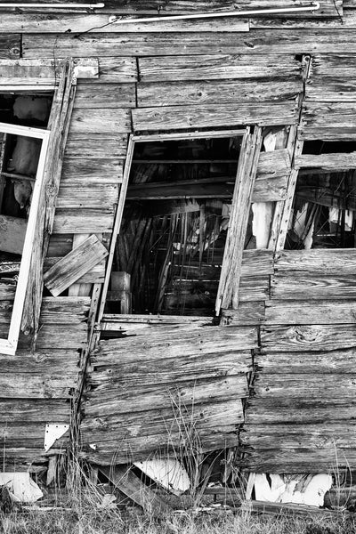 Black and white photograph of an old, abandoned wooden house along old Route 66 in Texola, Oklahoma, that has leaned sideways to an extreme angle.