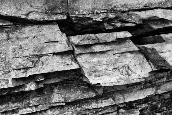 Black and white landscape photograph of fractured rock strata in the sheer wall of a mountain rock ledge.