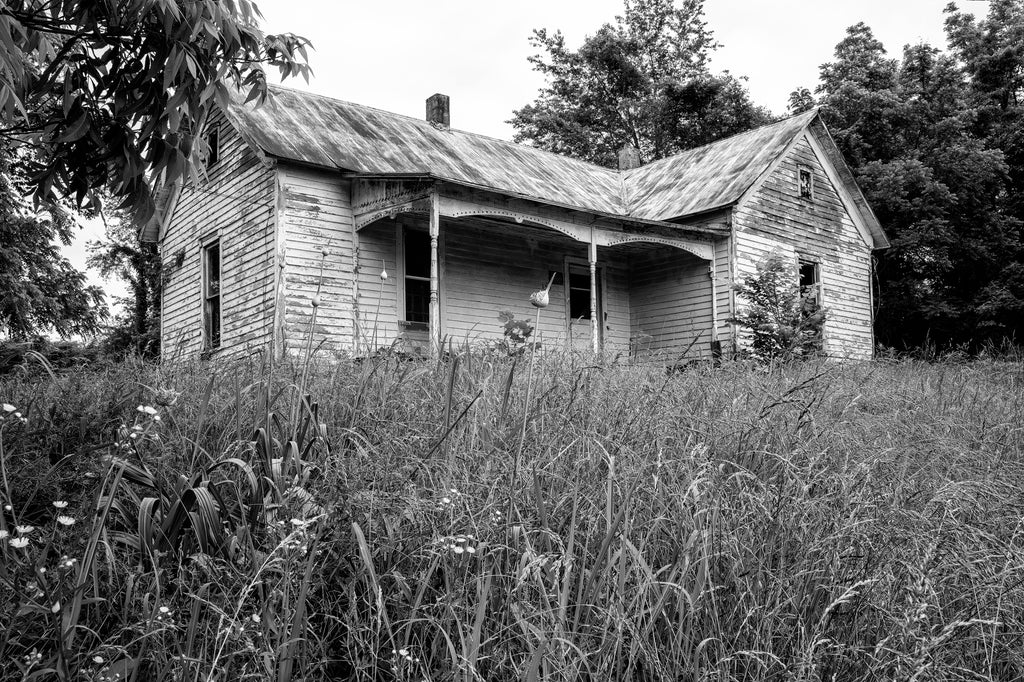 Black and white photograph of an old abandoned house on a hillside overlooking a mostly abandoned small town.