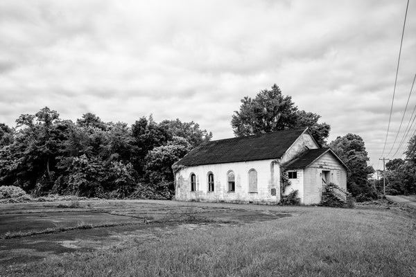 Black and white landscape photograph featuring an abandoned little white church in the American South.