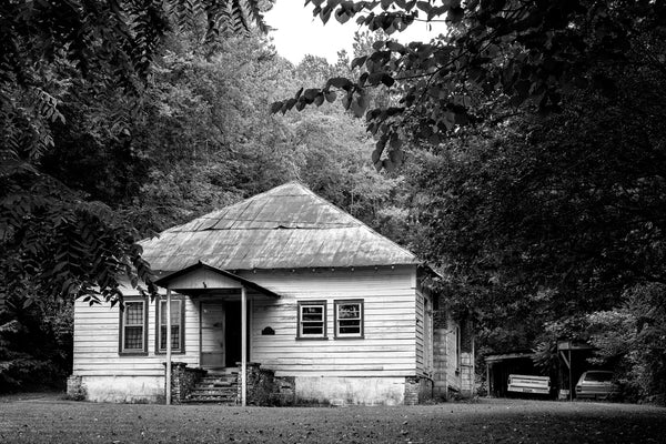 Black and white photograph of an abandoned farmhouse made poignant by the vintage pickup truck and station wagon left under a homemade carport in the back.